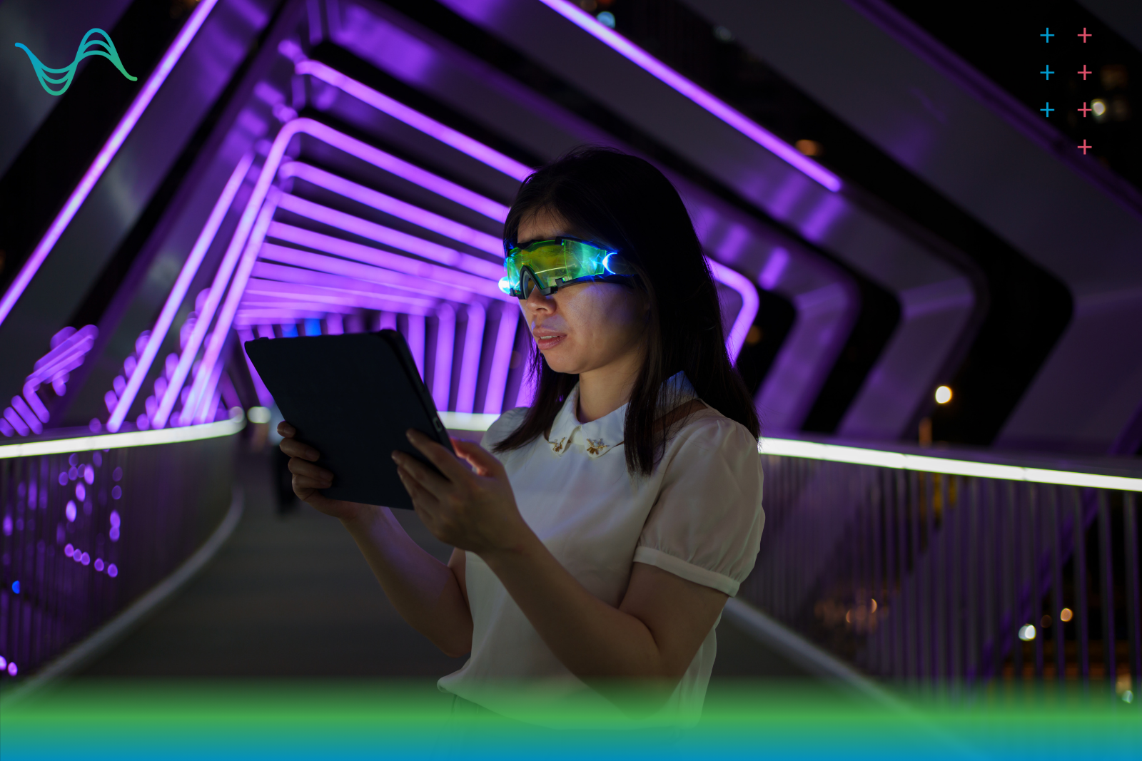 Picture of a young woman wearing a green viser looking at a digital tablet on a dark walkway with purple tube lights in the background.